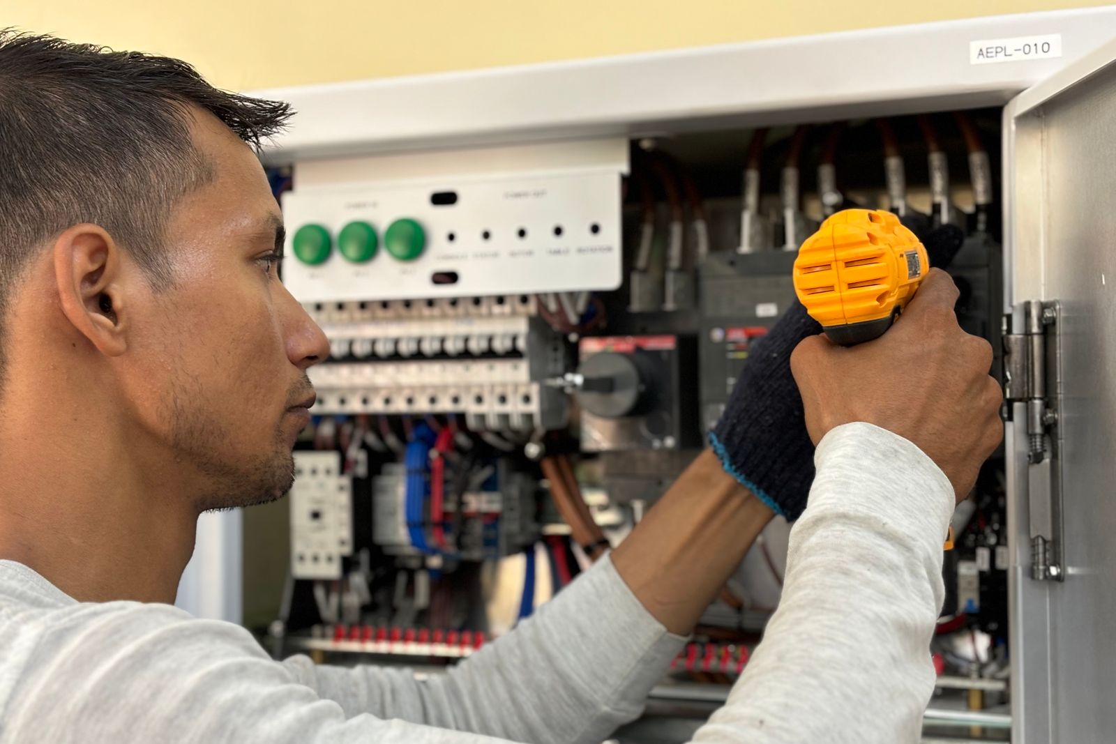 An electrician using a power drill while mounting equipment inside an electrical panel enclosure.